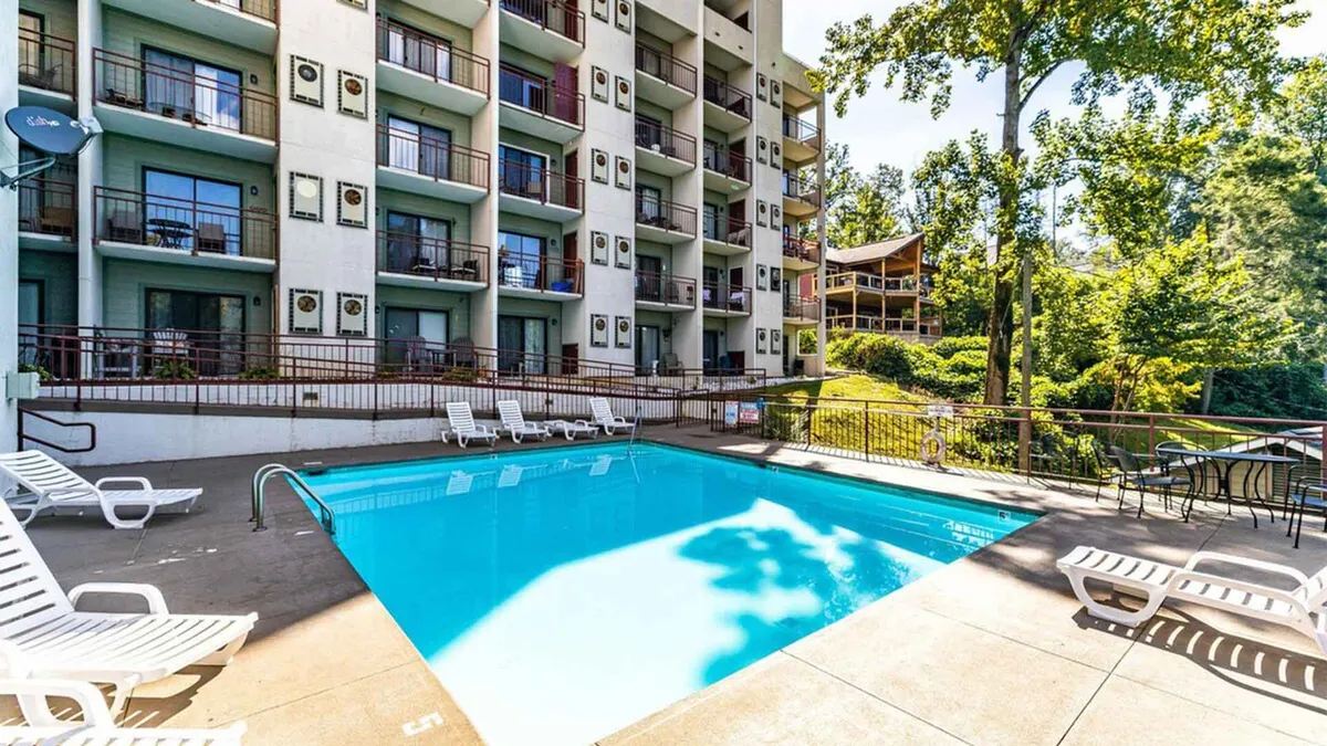 This image captures a resort-style swimming pool surrounded by inviting lounge chairs and balconies, all nestled amidst lush trees. The tranquil atmosphere is ideal for both relaxing swims and social gatherings, and the view of the balconies hints at the seamless connection between private accommodations and shared resort amenities.