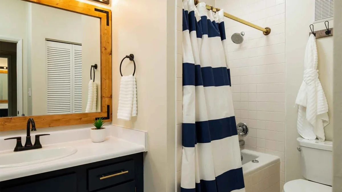 A fresh, modern bathroom featuring a large mirror above a stylish sink, a neatly hung shower curtain, and a pristine toilet. Soft lighting and thoughtful details create an inviting space for relaxation and self-care after a busy day.