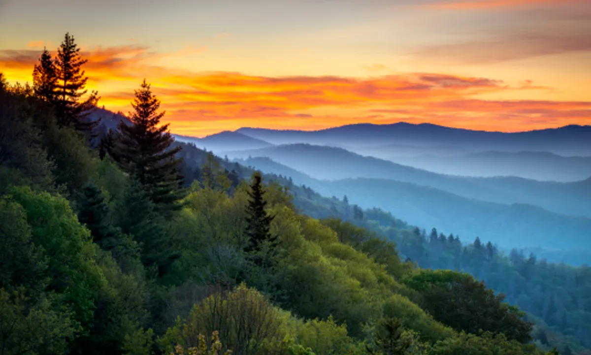 A spectacular view of a vibrant sunset over the rolling mountain ranges and dense forest, with warm, golden light casting a serene glow. The scene evokes peace, reflection, and awe at nature’s beauty—echoing the description of balcony moments.