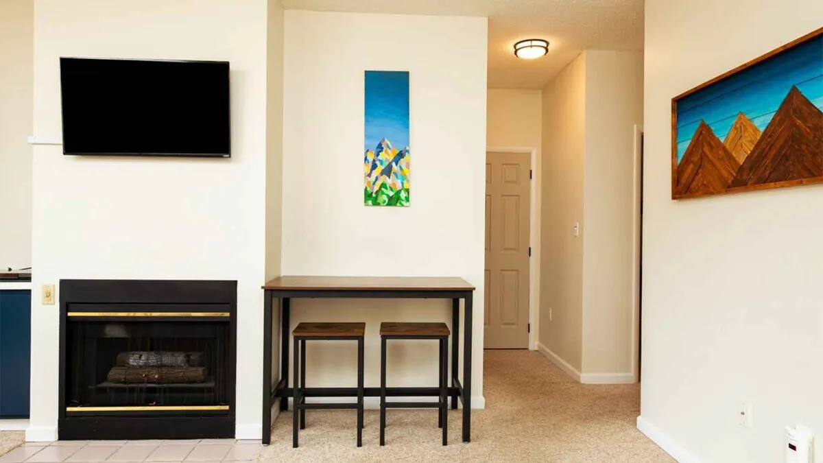 An inviting living area featuring a modern fireplace, tasteful artwork on the wall, and a cozy bar table with stools. The warm glow of the fire creates an atmosphere of comfort and relaxation, ideal for unwinding after a busy day.